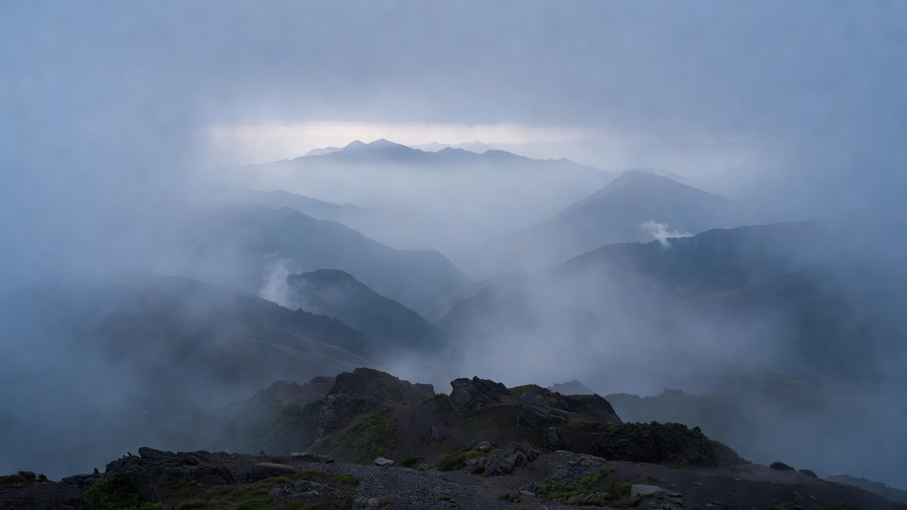 清晨高原山谷中的冷调雾气与层叠远山，近景碎石坡保留暗部细节